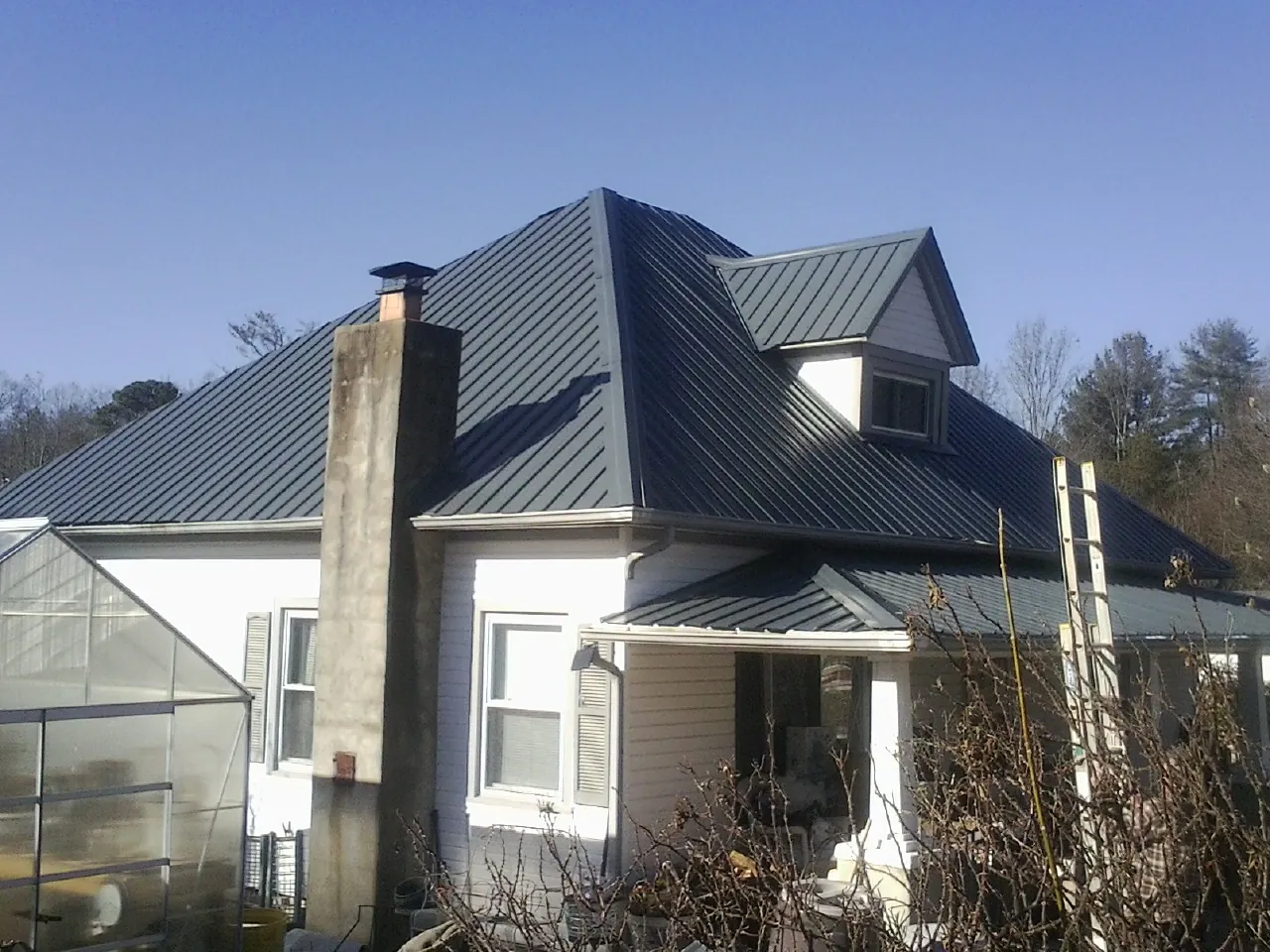 Dark blue standing seam metal roof on a white farmhouse with dormer — Slate & Tile Roof Repair by Roofing Brothers in Sangerfield