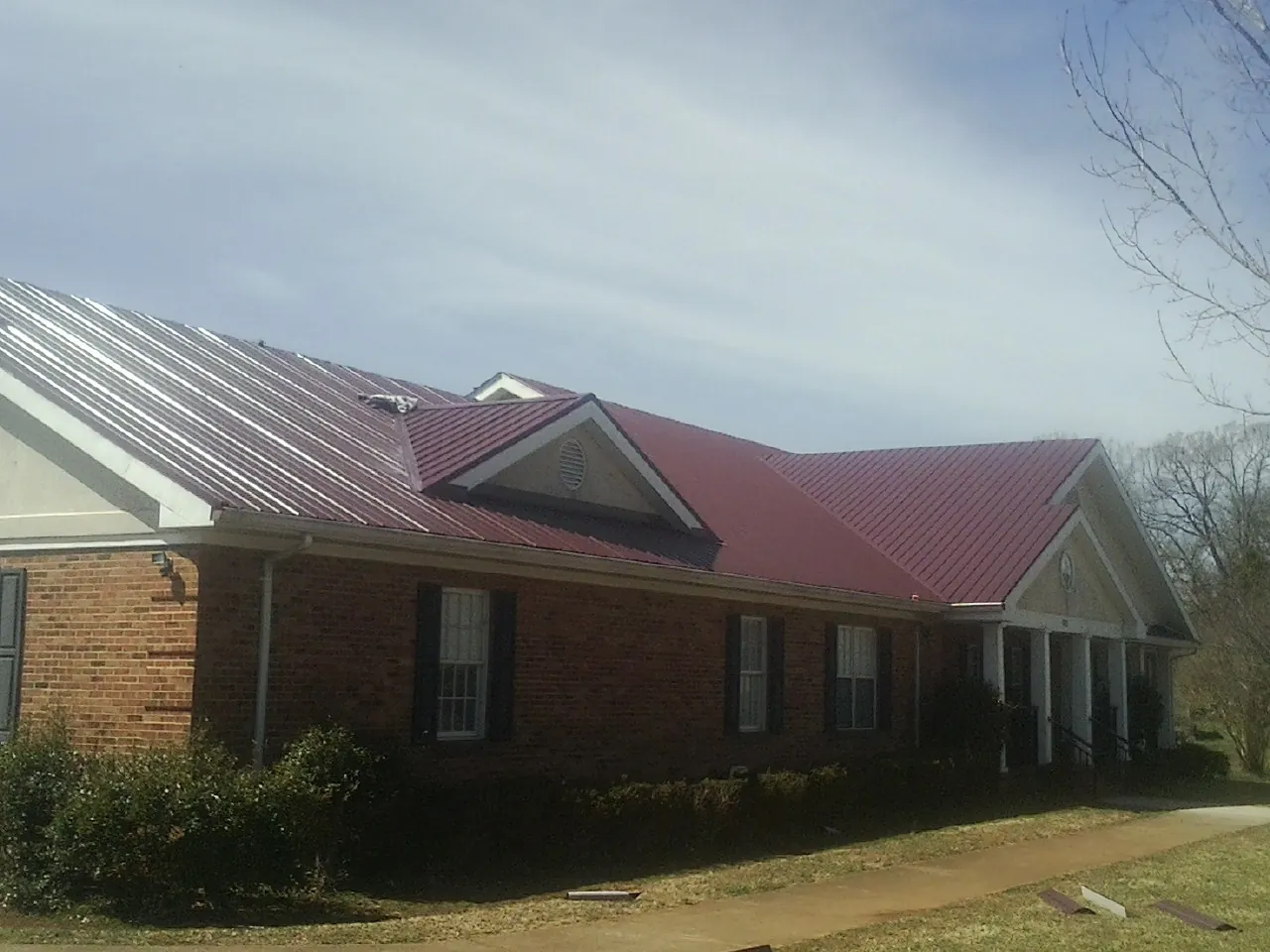 Red metal roof with gabled entries on a long brick building, from a Hail Damage Roof Repair job in Sangerfield