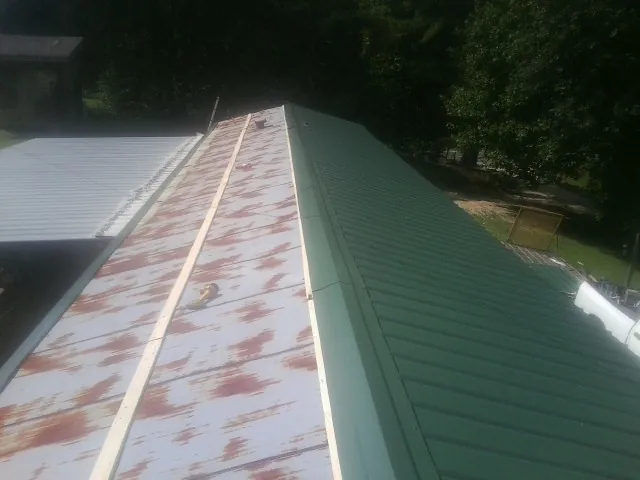Old rusted panels beside newly installed green metal roofing — Wind Damage Roof Repair by Roofing Brothers in Sangerfield
