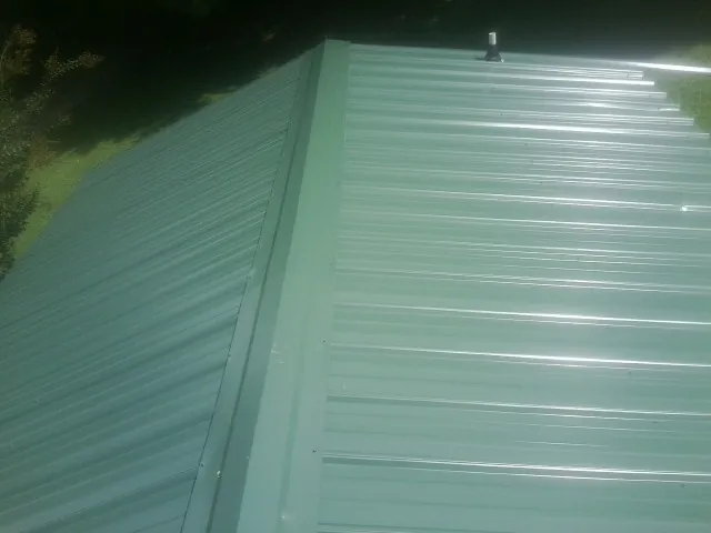 New green metal panels meeting at the ridge of a roof — Flat Roof Repair work by our crew in Sangerfield