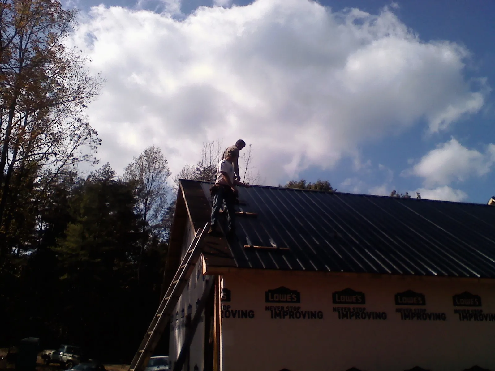Roofer fastening dark metal panels high against a cloudy sky, from a Roof Inspection job in Sangerfield