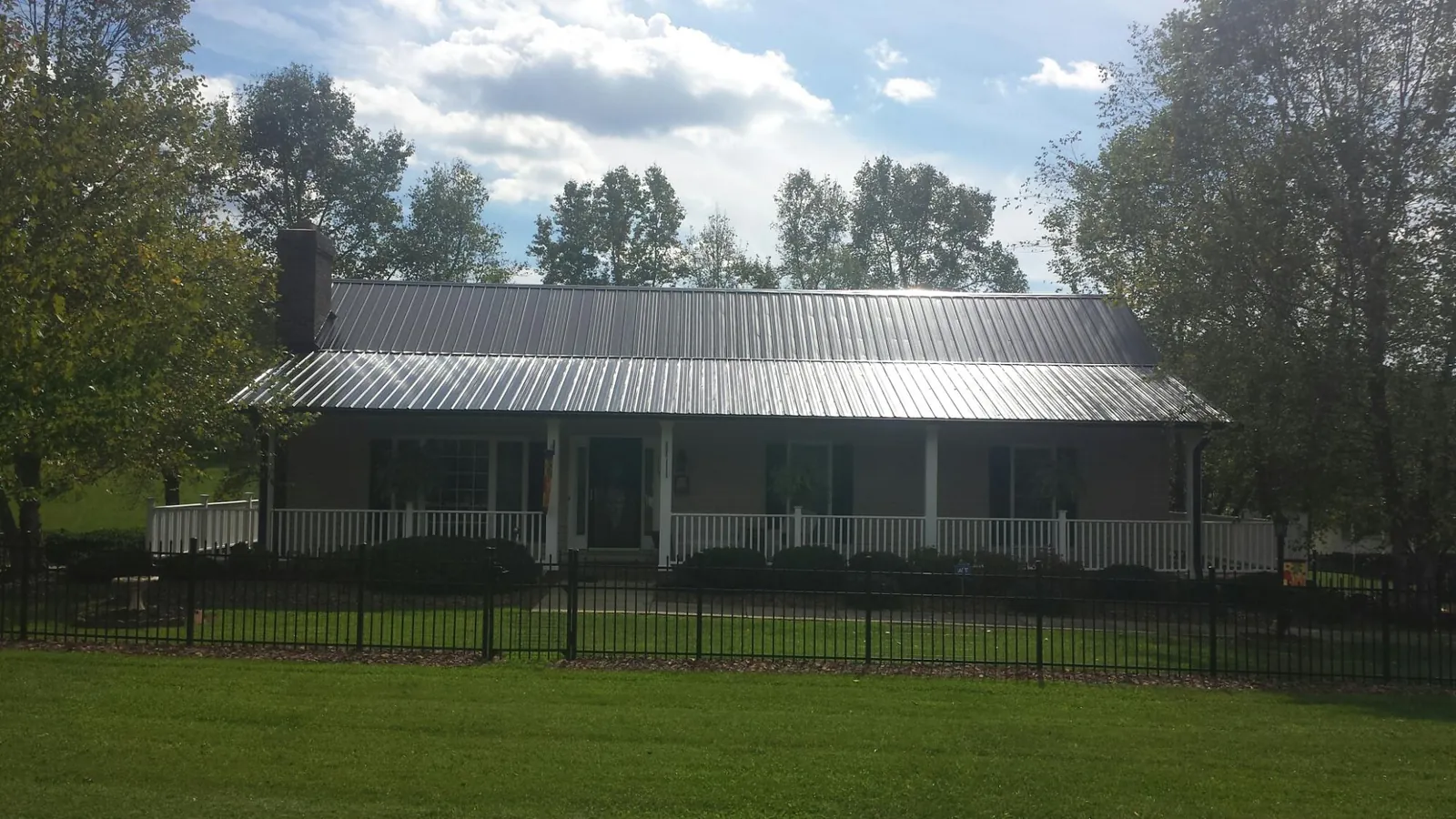 Gray metal roof on a brick ranch with a full width front porch — Gutter Guard Installation work by our crew in Sangerfield