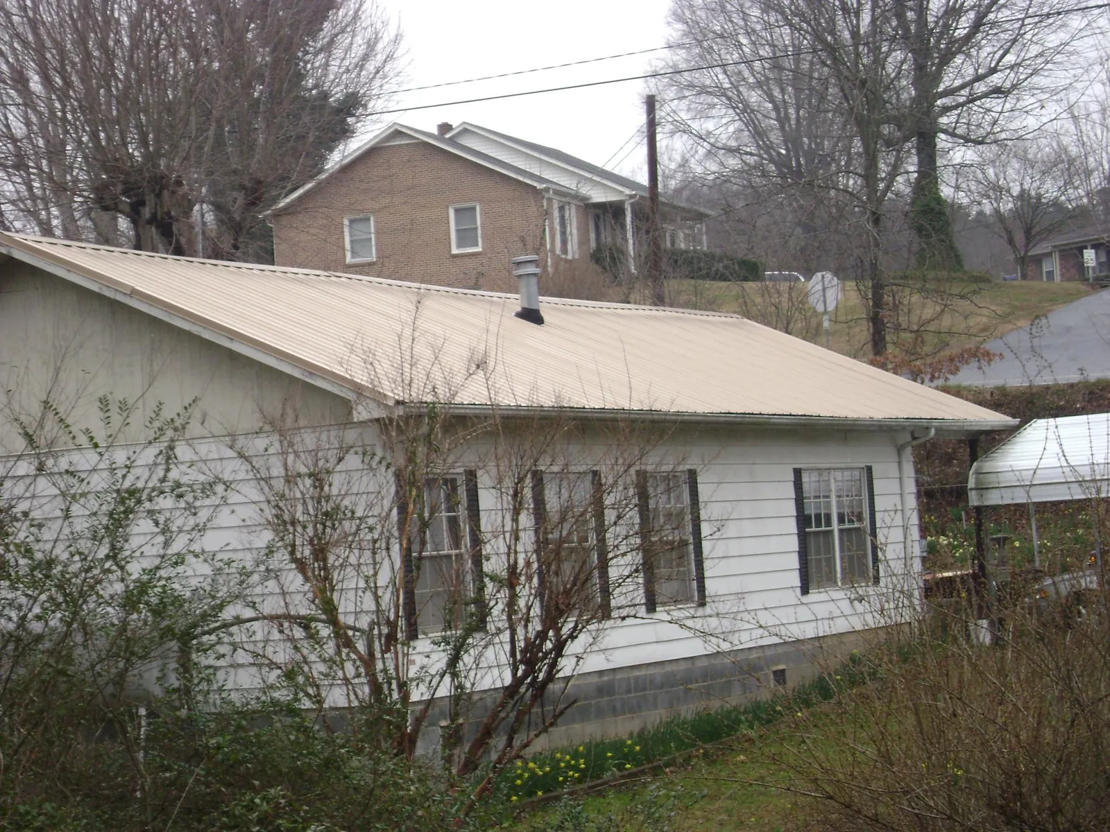 Tan metal roof on a white sided house set into a hillside — Commercial Roofing by Roofing Brothers in Sangerfield