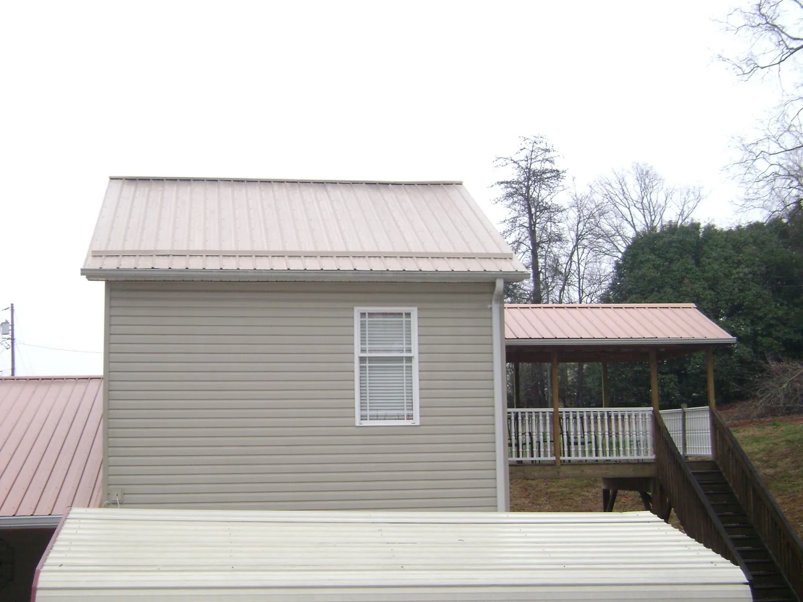 Tan metal roofs on a two story addition and attached porch, from a Roof Replacement job in Sangerfield